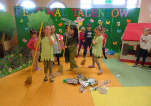 Dzieci śpiewają piosenkę, na środku tańczą trzy dziewczynki z miotłami wokół rozsypanych odpadków.
